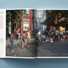 Texte: „THE UNITED STATES OF AMERICA, A portrait in the USA over a decade“. Menschen spielen und unterhalten sich auf einer belebten Straße.