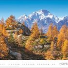 "NOVEMBER" steht in großen Buchstaben. Eine herbstliche Berglandschaft mit schneebedeckten Gipfeln und goldenen Bäumen.