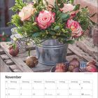 November-Tabelle mit Feiertagen, darüber ein Blumenarrangement: rosa Rosen, grüne Zweige, Mistelzweige in einem Metalltopf.