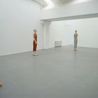 Vier schlichte Frauenfiguren in einem weißen, leeren Raum, jede in verschiedenen Farben gekleidet.