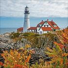 Leuchtturm auf Klippen am Meer, umgeben von herbstlichen Bäumen und einem Gebäude mit roten Dächern.