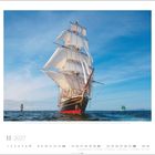 11 2027. Ein großes Segelschiff mit vollen weißen Segeln fährt auf ruhiger See unter klarem blauem Himmel.