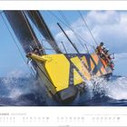 November. Vor einem gelben Segelschiff mit schwarzem Muster sitzen Menschen. Wellen spritzen um das Boot.