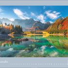 November 2027. Ein klarer See spiegelt bunte Herbstbäume und Berge bei blauem Himmel wider.