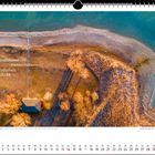 "Am azurblauen Ufer leuchten die Bäume bernsteinfarben im Abendlicht." Luftaufnahme mit Ufer, Bäumen und einem Haus im Herbst.