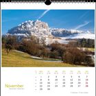 November, Kalender mit verschneiter Landschaft, Hügel im Hintergrund, Bäume im Vordergrund, blauer Himmel.