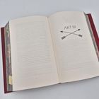Der Text "AKT III" steht über zwei gekreuzten Pfeilen auf einer Buchseite mit dekorativem Randmuster.