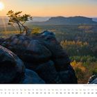 Text: "November, Spätherbstliche Sächsische Schweiz mit Blick vom Gohrisch auf den Pfaffenstein mit Barbarine."  
Blick auf Felsen, Baum und Wald im Sonnenuntergang.