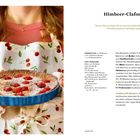Himbeer-Clafoutis Rezept. Frau in rotem Oberteil hält eine mit Puderzucker bestäubte Himbeertarte in blauer Form.