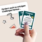 Text: "Fordert euch zu witzigen Challenges heraus ..." Zwei Karten mit einer Hand gehalten, umgeben von grafischen Elementen.