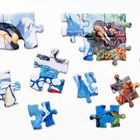 Zerstreute Puzzle-Teile mit Motiven von Pinguinen, Schnee, Wasser und farbenfrohen Unterwasserszenen.