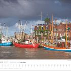 Text: "November 2027 | KÜSTENLAND Meer erleben." Fischerboote liegen an einem Hafen mit Backsteingebäuden.