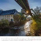 "November 2027, Wuppertal, Alte Kornmühle. Eine Schwebebahn überquert einen Fluss bei Sonnenuntergang."