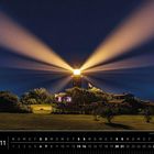 Dänemark 11. Ein Leuchtturm strahlt nachts hell in den Himmel, umgeben von Bäumen und einem Gebäude.