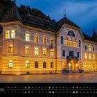 Text: "Liechtenstein 11, Regierungsgebäude in Vaduz." Beleuchtetes Gebäude mit verziertem Dach bei Dämmerung.