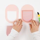 Zwei Hände arbeiten mit rosa Papierformen, neben einer gelben Kleberflasche.