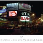 Leuchtende Werbetafeln mit den Texten: Samsung, TDK, Sanyo, Coca-Cola Vanilla über einer belebten Kreuzung bei Nacht.