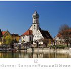 "Wasserburg" mit Kalenderdaten darunter. Uferansicht mit Architektur im traditionellen Stil, Bäume und Boote im Vordergrund.