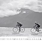Kalenderseite mit Dezemberdaten, zwei Radfahrer in schwarz-weiß auf einer Bergstraße, Berge und Wolken im Hintergrund.