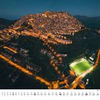 Kalenderseite mit Zahlen 1 bis 31. Nachtaufnahme einer beleuchteten, dichten Bergstadt mit Fußballfeld in Italien, Gangi.