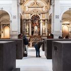 Ein Raum mit hohen Decken, Marmorbögen, Statuen und großen, dunklen Quadern, in die Menschen hineinschauen.