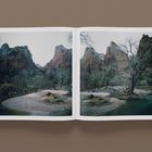 Doppelseitige Fotografie in einem Buch. Sie zeigt eine Flusslandschaft mit Bäumen und hohen Bergen im Hintergrund.