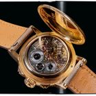 Uhrwerk mit sichtbaren Zahnrädern und einer geöffneten goldenen Rückseite, braunes Lederarmband mit eingeprägten Zahlen.