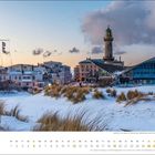 Dezemberkalenderbild mit verschneiten Dünen, Gebäuden, einem Leuchtturm und einem modernen Gebäude an der Küste.