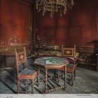 12 2023. Verwitterter Raum mit Holzmöbeln, zwei Stühlen, kleinem Tisch, einem alten Buch und einem Kronleuchter.