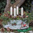 Vier Kerzen, eine brennend, in Tannengesteck mit Zapfen und roten Beeren in bemalter Schale, Holzpferd im Vordergrund.