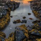 Kalenderblatt für Dezember 2021, Küstenlandschaft bei Sonnenuntergang, Felsen mit gelbem Seetang und ruhiges Wasser.