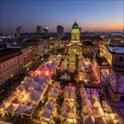 Ein Weihnachtsmarkt bei Abenddämmerung, mit vielen beleuchteten Ständen und einem großen, geschmückten Baum in der Mitte.