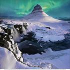 Dezember 2023. Verschneite Landschaft mit Berg und Wasserfall, darüber grüne Polarlichter am Himmel.