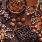 Unterschiedliche Schokoladenarten, Nüsse, Kakaopulver, Löffel und Trüffel auf braunem Hintergrund arrangiert.