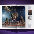 Eine aufgeschlagene Buchseite zeigt ein Basketballspiel mit Spielern in grünen und weißen Trikots. Links sind weitere Texte.