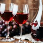 „Ein gutes Glas Wein ist geeignet, den Verstand zu wecken.“ Zwei Weingläser, gefüllt mit Rotwein, mit Trauben im Hintergrund.