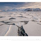 "Dezember" steht in der Mitte unten. Gecracktes Packeis erstreckt sich vor schneebedeckten Bergen unter einem bewölkten Himmel.
