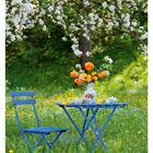 11. März, blauer Tisch und Stuhl auf Wiese, Vase mit orangenen Blumen, blühender Apfelbaum im Hintergrund.