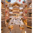 11 MÄRZ. Eine moderne Bibliothek mit hohen Bücherregalen, leuchtenden Stufen und bunten Kugeln an der Decke.