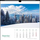Kalenderseite mit Dezember. Schneebedeckte Tannen, blauer Himmel und ein weiter Blick über eine Landschaft.
