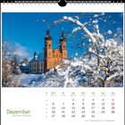 Kalenderseite für Dezember. Schneebedeckter Baum vor einer Kirche mit zwei Türmen unter blauem Himmel.