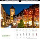 Dezemberkalender mit beleuchteter Altstadt bei Nacht. Lichter schmücken Bäume, und ein Turm steht im Hintergrund.