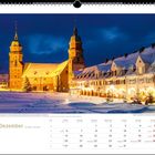 Dezemberkalender: Schnee bedeckt einen Marktplatz mit Kirche und beleuchteten Häusern. Festlich beleuchtet, winterliche Atmosphäre.