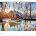 Dezemberkalenderblatt mit winterlicher Szene, gefrorener Fluss, umgeben von Bäumen und einem Holzhaus im Sonnenuntergang.