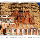 November. Kloster in Nepal, gebaut in Felswand mit bunten Gebetsfahnen und traditionellen Gebäuden in rötlichem Gestein.