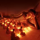 Mönche meditieren bei Kerzenlicht vor einer großen liegenden Buddha-Statue in einem dunklen Raum.