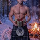 Dezember. Ein lächelnder Mann in Weihnachtsmütze und Kilt hält ein Geschenk, im verschneiten Wald vor einem Feuer.