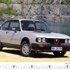 "DEZEMBER 1-31, Alfa Romeo Alfasud Ti 1.5 QV Baujahr 1982." Ein silbernes Auto vor einem See und Felswand.