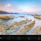 "Neuseeland 12, Kaikoura Halbinsel." Kalender mit felsiger Küste im Vordergrund und Bergen im Hintergrund bei Sonnenuntergang.