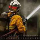 Kalender mit Zahlen: 1-31 und Wochentagen. Ein Feuerwehrmann in gelber Uniform löscht mit einem Schlauch Wasser.